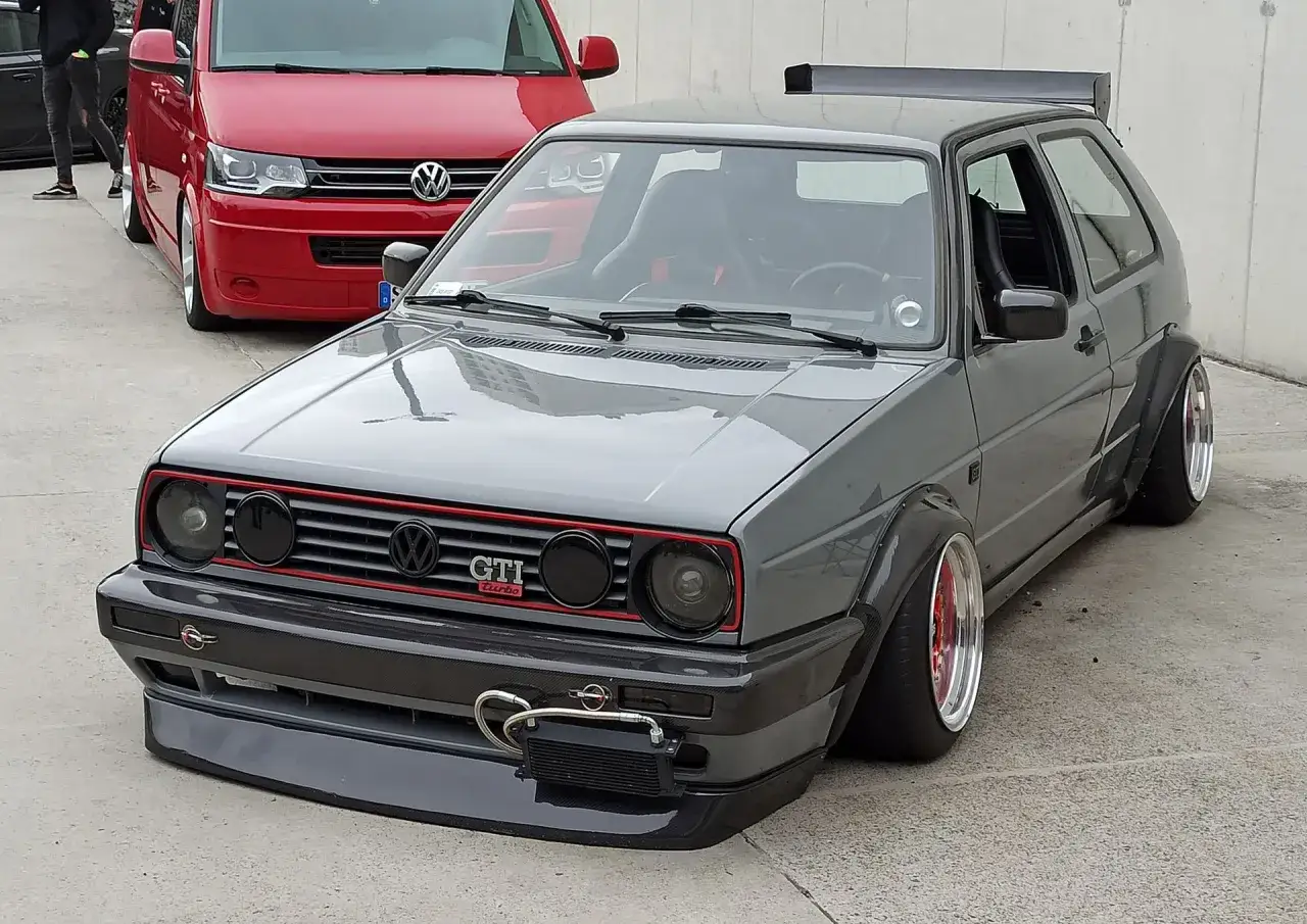 Szary, zmodyfikowany Volkswagen Golf GTI z szerokimi błotnikami i spojlerem.