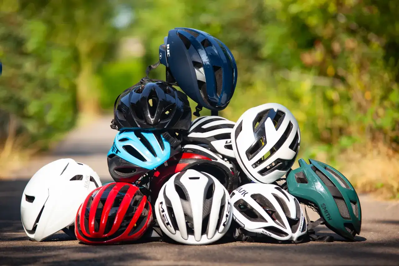 Stos kasków rowerowych, gotowych do testów ADAC. Różne kolory i modele, od białego po granatowy.