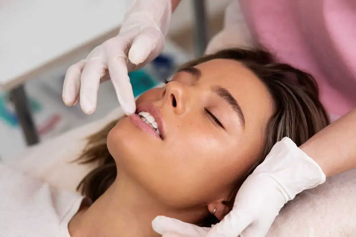 Kobieta z zamkniętymi oczami, której usta są dotykane przez ręce w białych rękawiczkach.