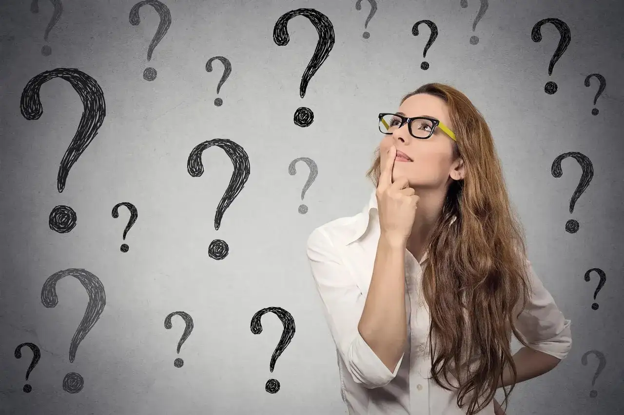 Kobieta w okularach z palcem przy ustach, otoczona znakami zapytania.