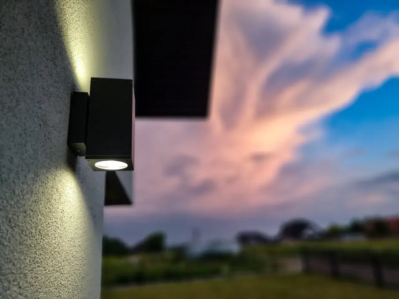 Nowoczesne lampy zewnętrzne na dom oświetlają ścianę, tworząc nastrojowy klimat przy zachodzącym słońcu.