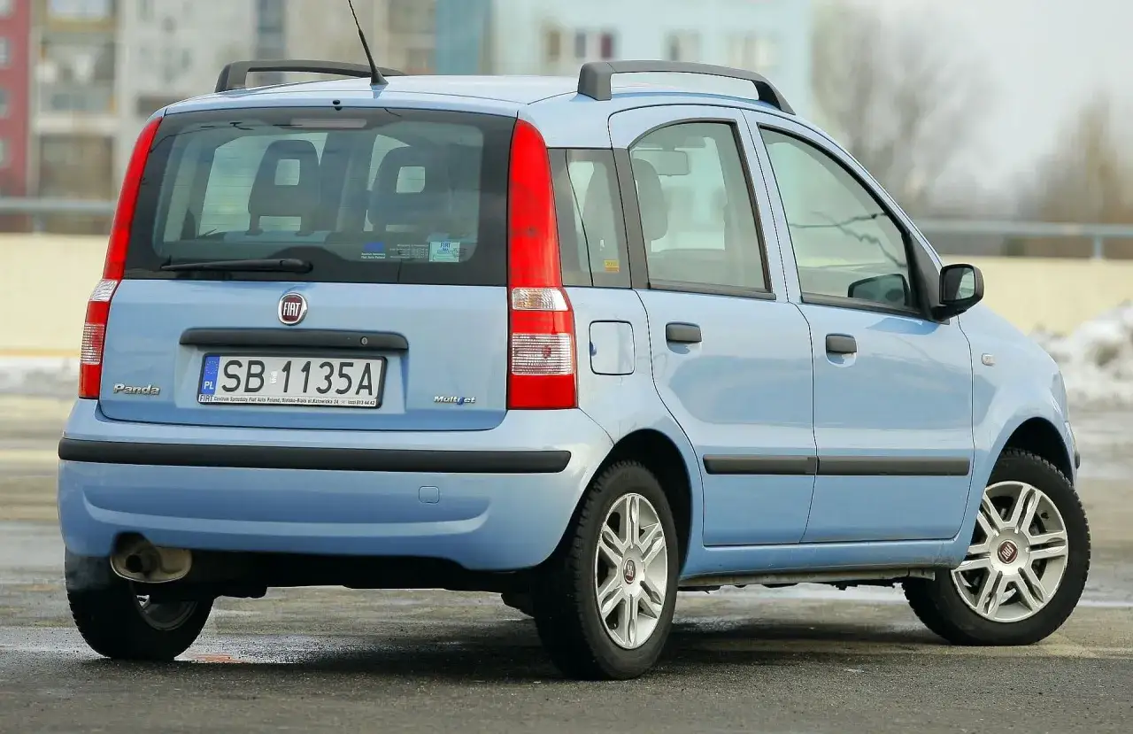 Błękitne małe auto Fiat Panda z automatyczną skrzynią biegów, idealne do 10 tys. zł, na tle miejskiego krajobrazu.