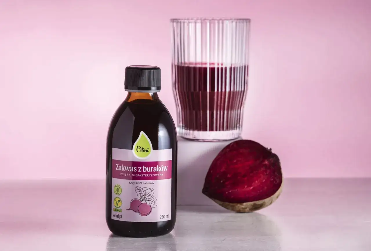 Butelka zakwasu z buraków Olini, szklanka z napojem i połówka buraka. Zastanawiasz się, ile zakwasu z buraka dziennie?