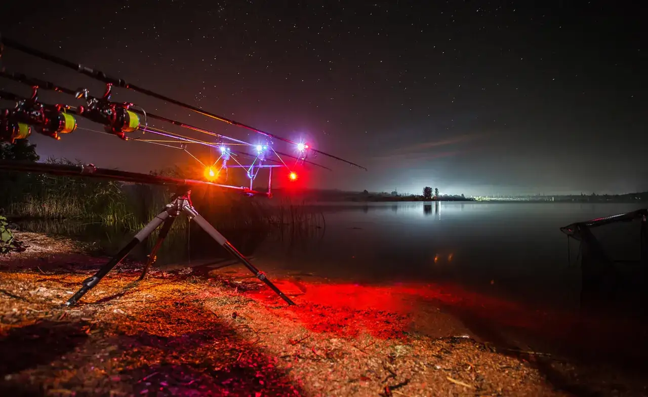 Nocne łowienie karpi. Wędki na podpórce z sygnalizatorami brań, jezioro i gwiazdy. To jak zrobić świetlik na ryby.