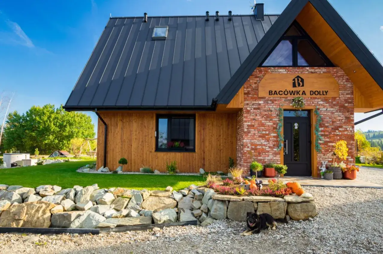 Urocza bacówka w Białce Tatrzańskiej, "Bacówka Dolly", z kamiennym cokołem i drewnianą elewacją. Przed domem leży pies.