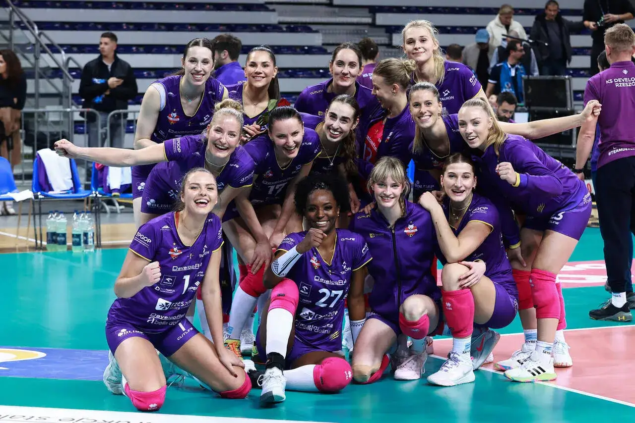Uśmiechnięte siatkarki Savino Del Bene Scandicci w fioletowych strojach świętują zwycięstwo.