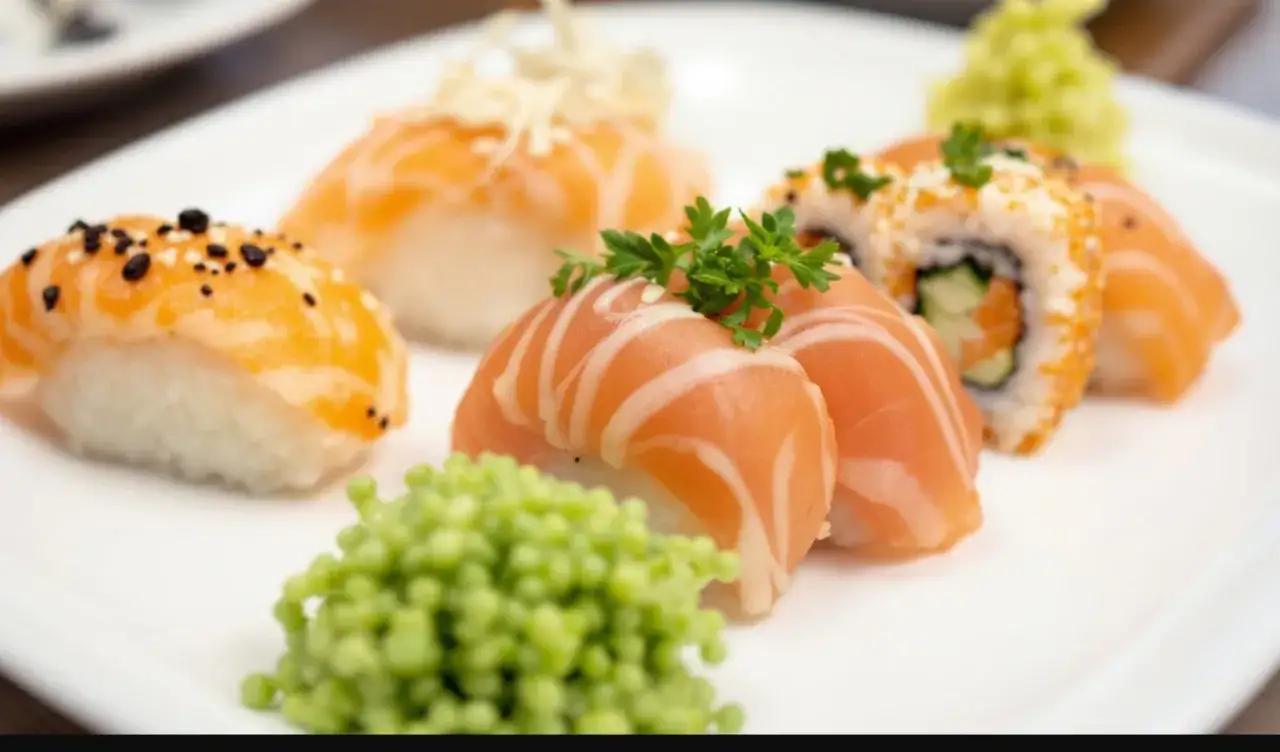 Talerz z różnorodnym nigiri sushi z łososiem, posypane sezamem i ozdobione natką pietruszki. Obok porcja zielonego wasabi.