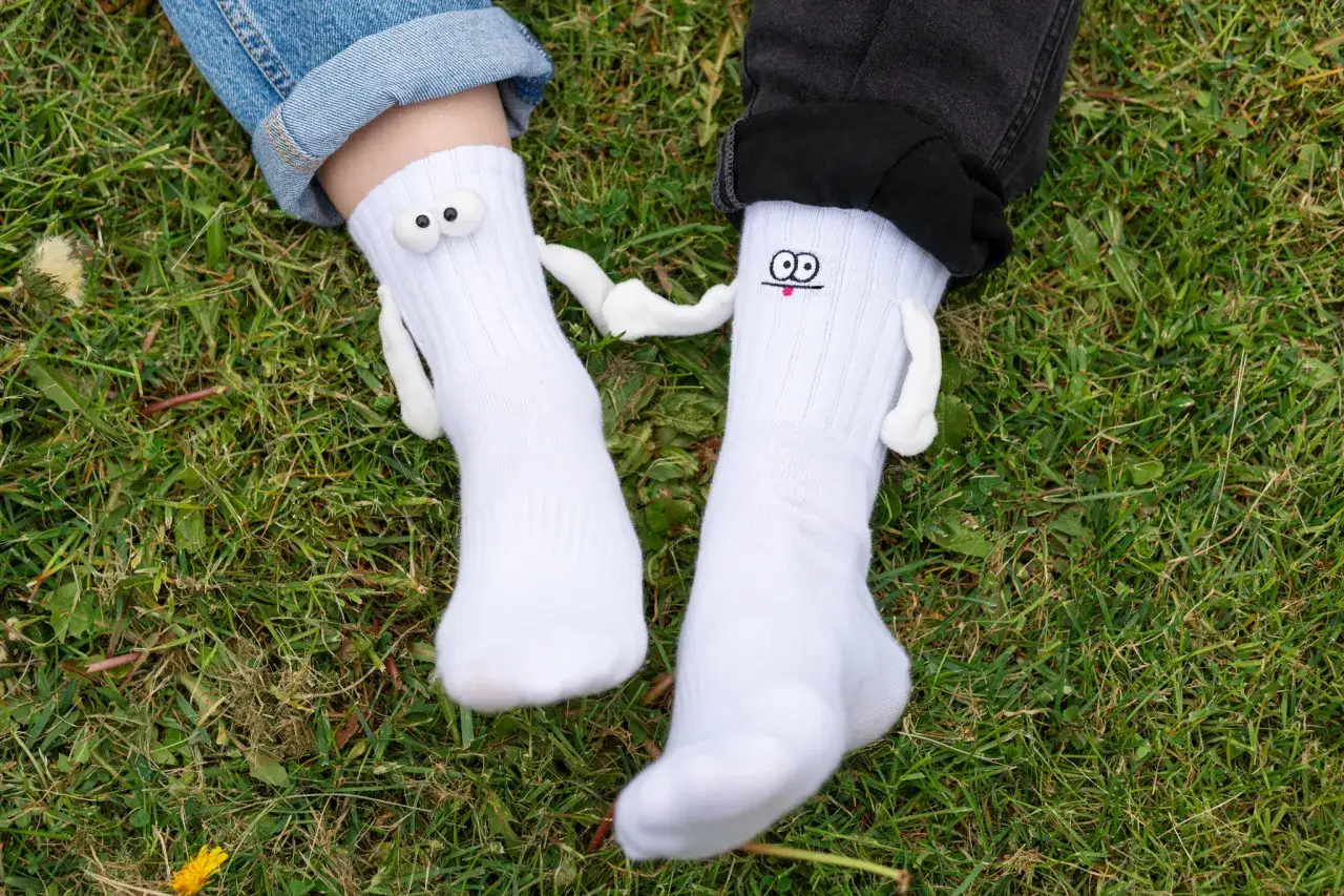 Dwie nogi w białych skarpetkach z zabawnymi buźkami, leżące na trawie.