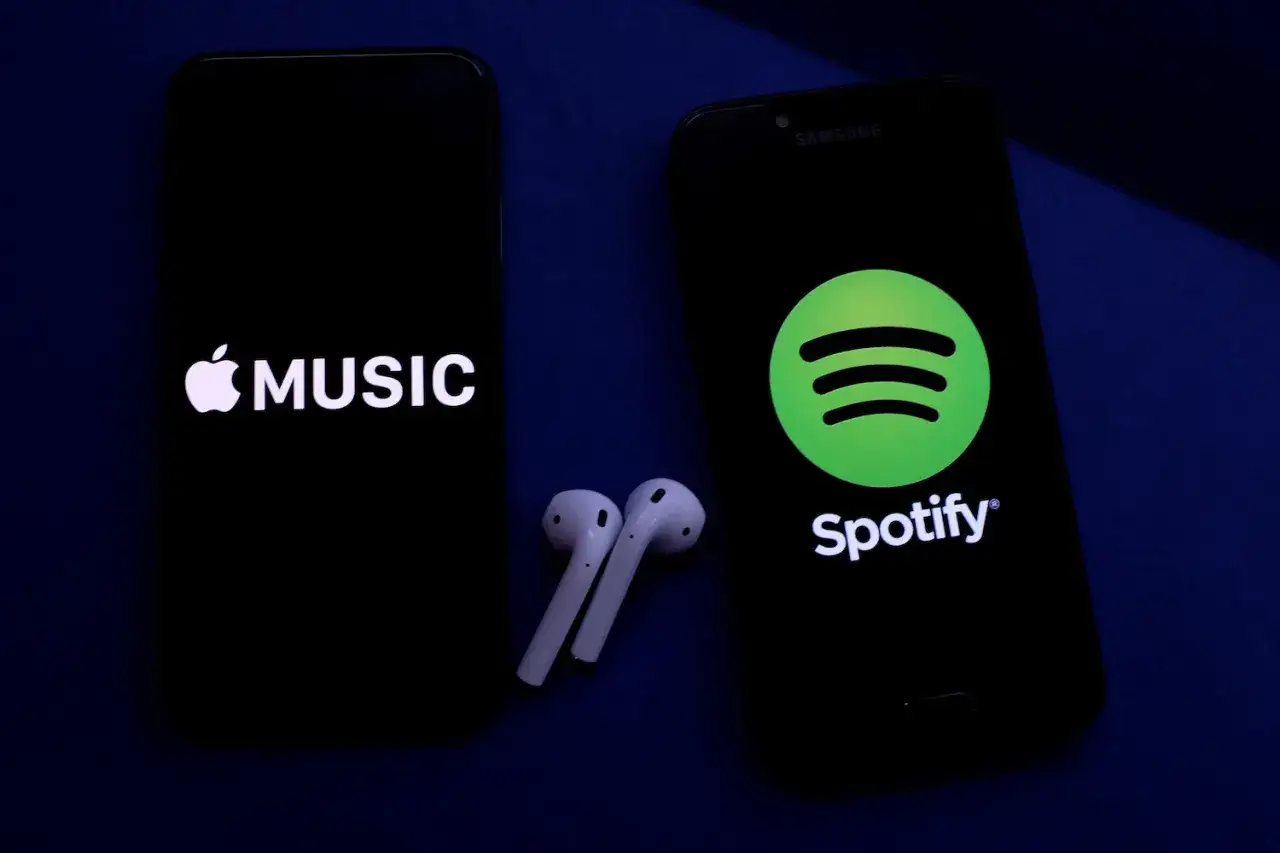 Dwa smartfony z logotypami Apple Music i Spotify, obok słuchawki bezprzewodowe.
