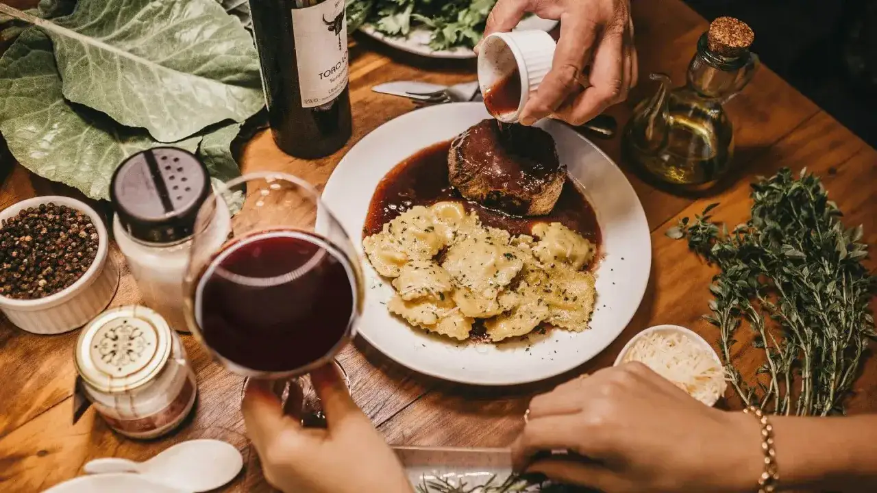 Elegancka kolacja z ravioli i wołowiną w sosie. Idealne pytanie: jakie wino do gotowania? Czerwone wino i świeże zioła dopełniają atmosferę.