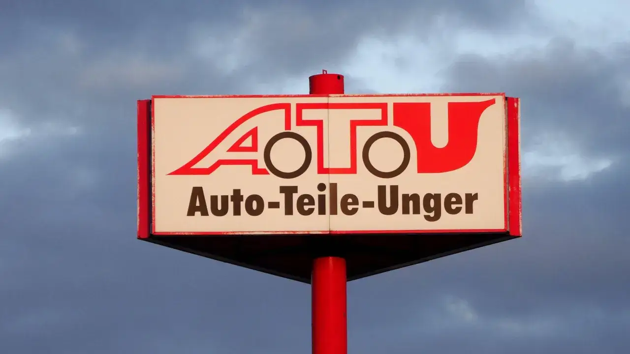 Schild mit rotem Schriftzug "A.T.U. Auto-Teile-Unger" vor bewölktem Himmel.