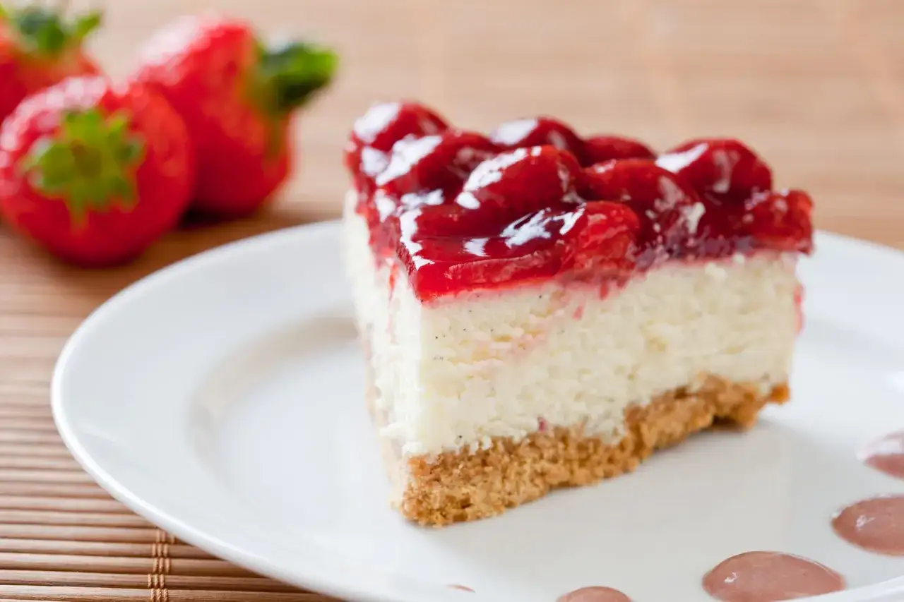 Pyszny sernikobrownie z truskawkami na białym talerzu, obok świeże truskawki.