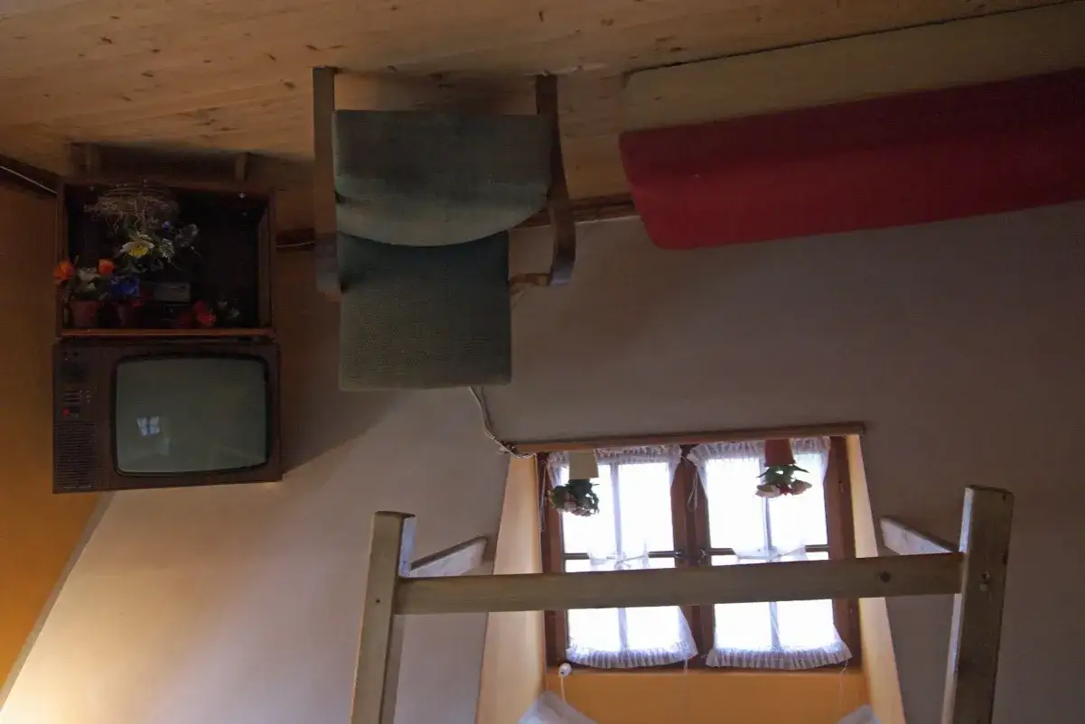 Wnętrze domu do góry nogami w Szymbarku: odwrócony telewizor, krzesło i łóżko.