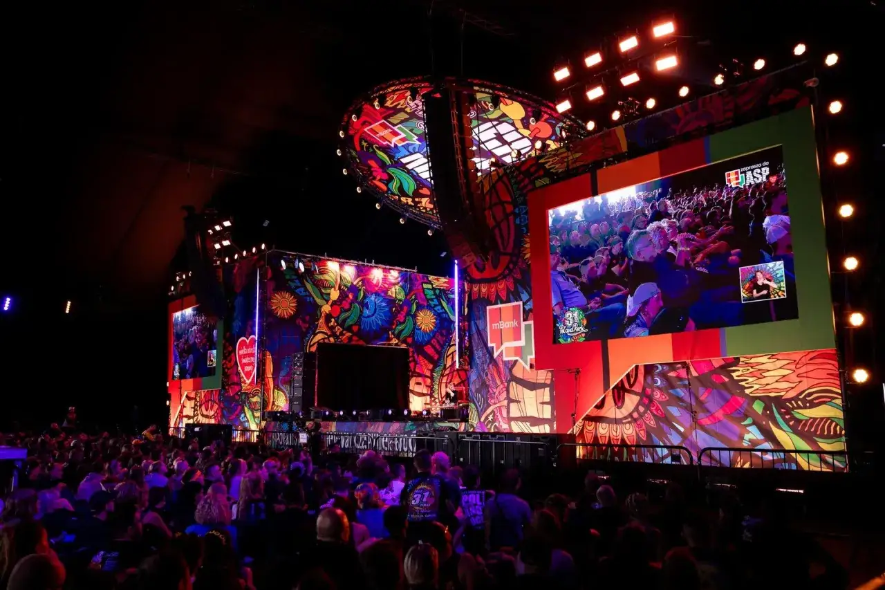 Kolorowa scena festiwalu Poland Rock 2026 z wielkim ekranem pokazującym publiczność. Tłum widzów wpatrzony w widowisko.