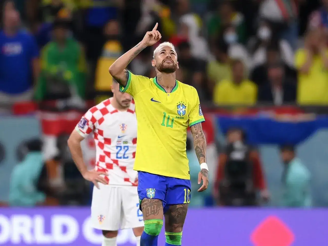 Neymar w żółtej koszulce Brazylii z podniesionym palcem, na tle stadionu.