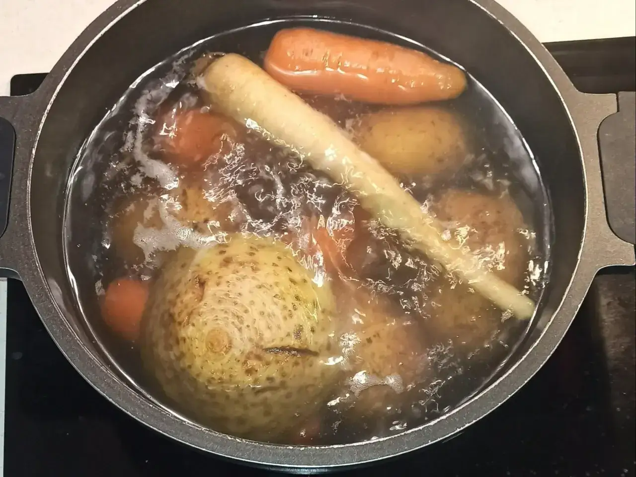 Warzywa (marchew, pasternak, ziemniaki, seler) gotujące się w garnku z wodą.