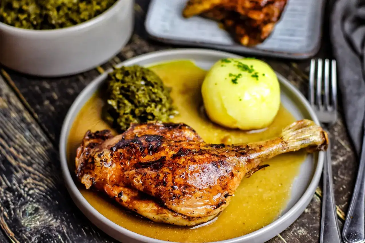 Gebratene Entenkeule mit Klößen und grüner Soße auf einem Teller.