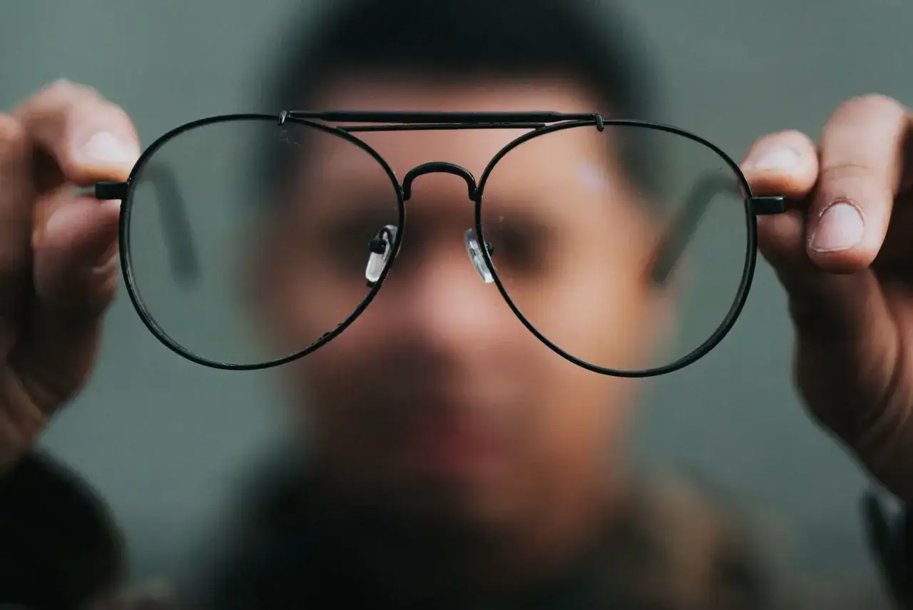 Osoba trzyma okulary przed twarzą. Chcesz wiedzieć, co zrobić, żeby nosić okulary?