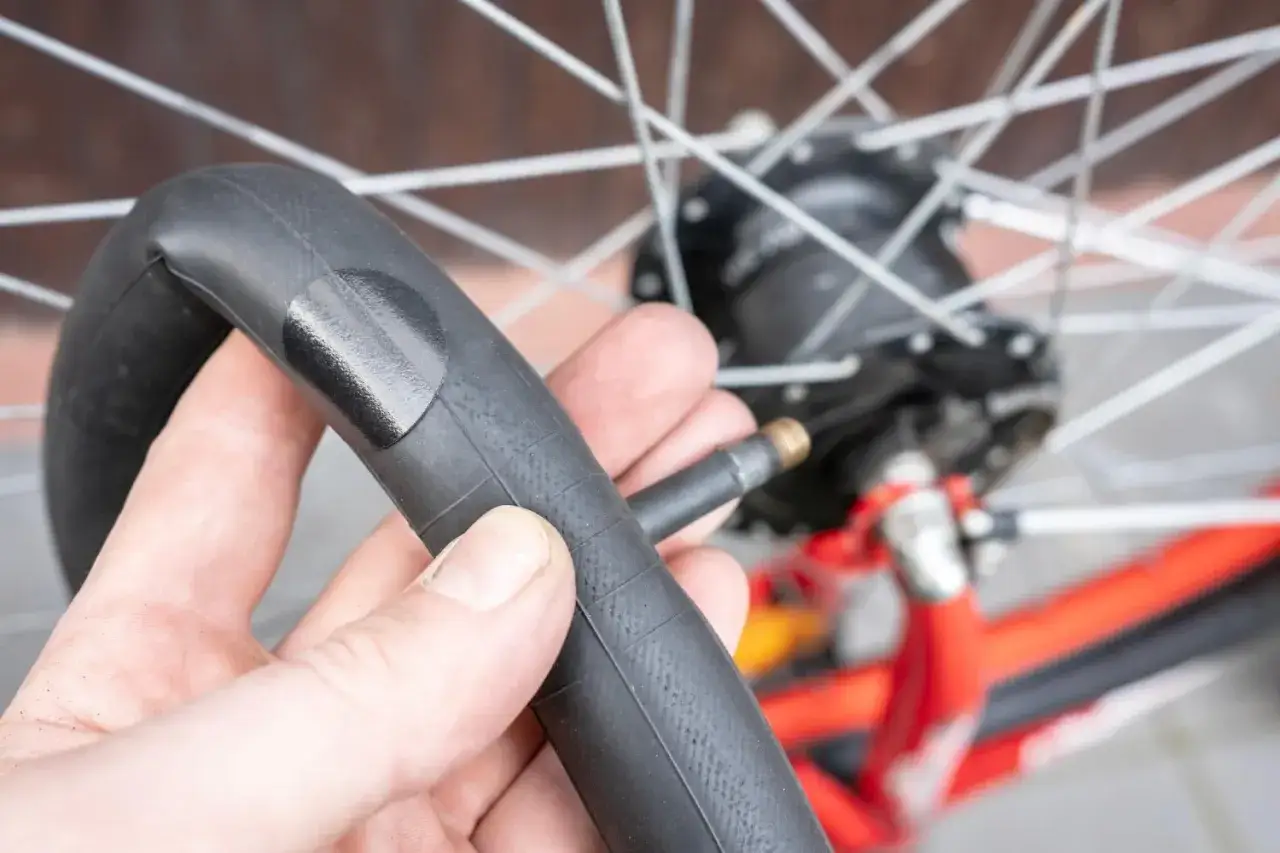 Dłoń trzyma załatany dętkę rowerową, gotową do montażu. Koło rowerowe w tle.