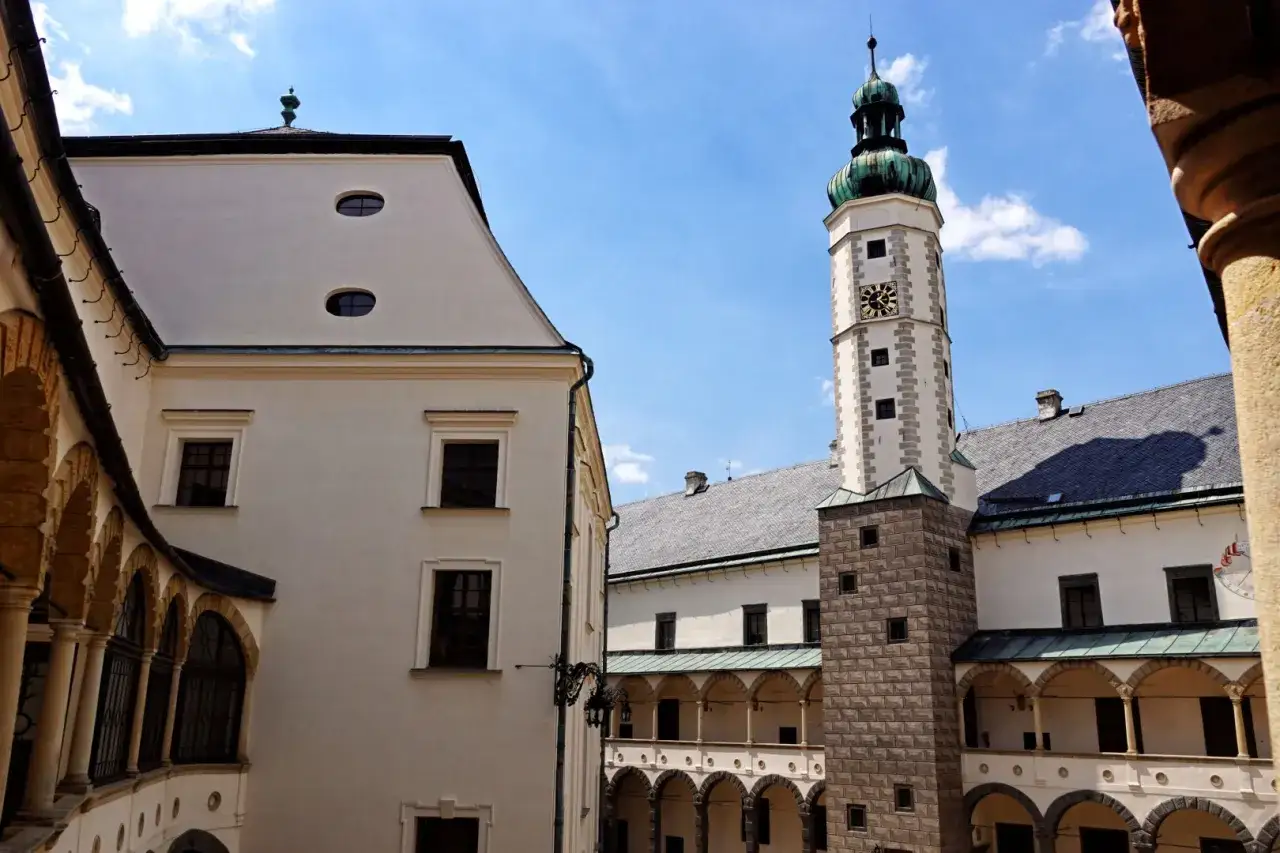 Dziedziniec zamku w Bruntalu, Czechy. Białe mury, arkadowe krużganki i wysoka wieża zegarowa pod błękitnym niebem.