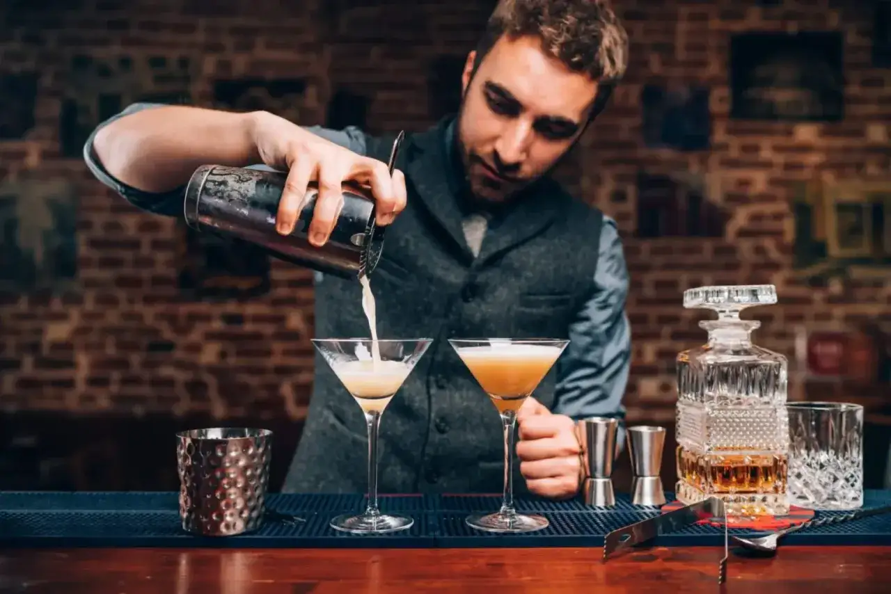 Barman przelewa drinka do kieliszka, tworząc idealną piankę z białka. Poznaj przyczyny mętnienia drinków typu sour.