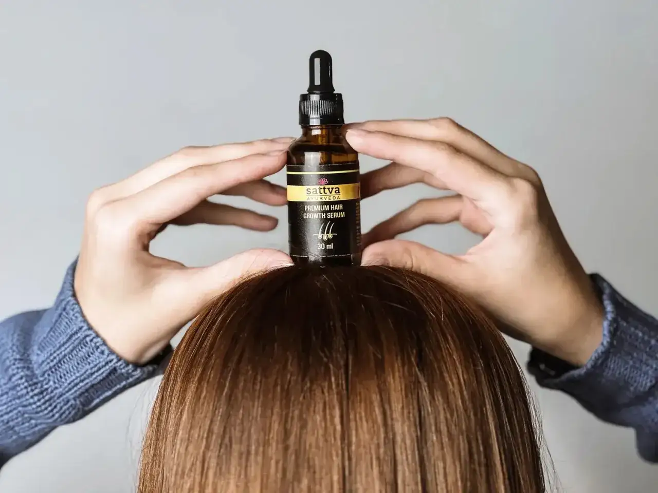 Dłonie trzymają buteleczkę z serum do włosów Sattva Ayurveda. Czy serum do włosów się spłukuje? To pytanie zadaje sobie wiele osób.