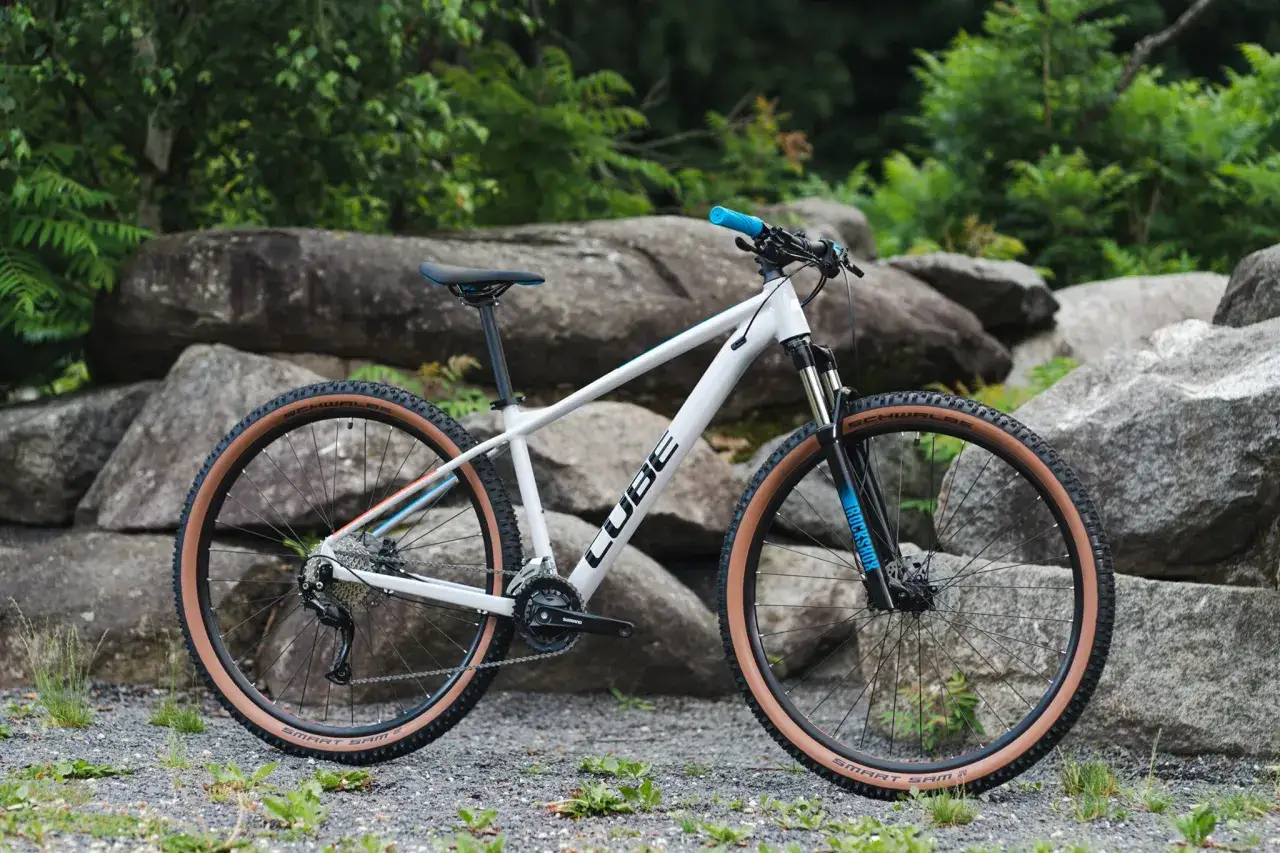 Biały rower Cube z brązowymi oponami, idealny jako rower na długie trasy. Wyposażony w amortyzator RockShox i napęd Shimano.