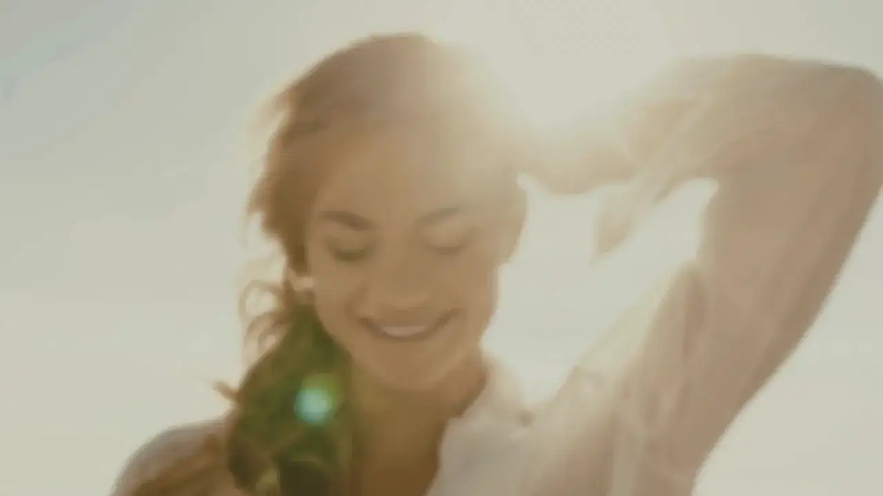 Lächelnde Frau im Sonnenlicht mit erhobener Hand.