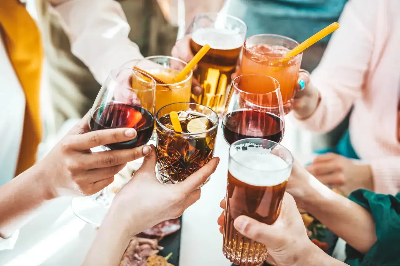 Ręce wznoszą kieliszki z winem, drinkami i piwem, celebrując wspólne chwile.