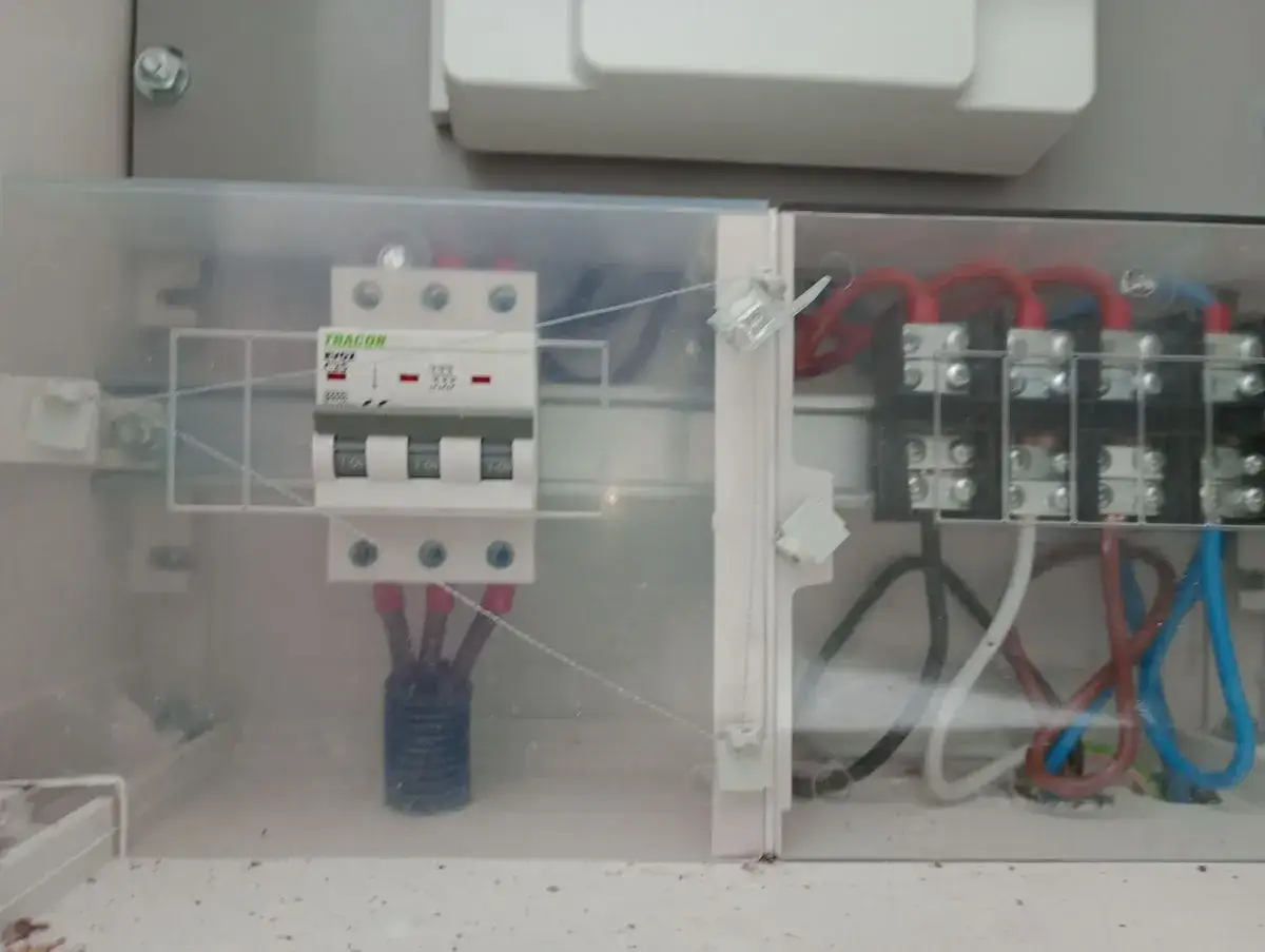 Trzybiegunowy wyłącznik nadprądowy w obudowie z przezroczystego plastiku, podłączony do przewodów.