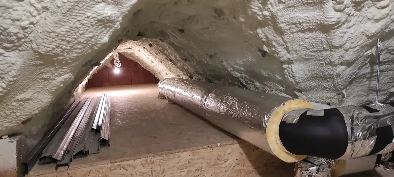 Izolacja kanałów wentylacyjnych w poddaszu, pokrytym pianką PUR. Widać metalowe profile i oświetlenie.