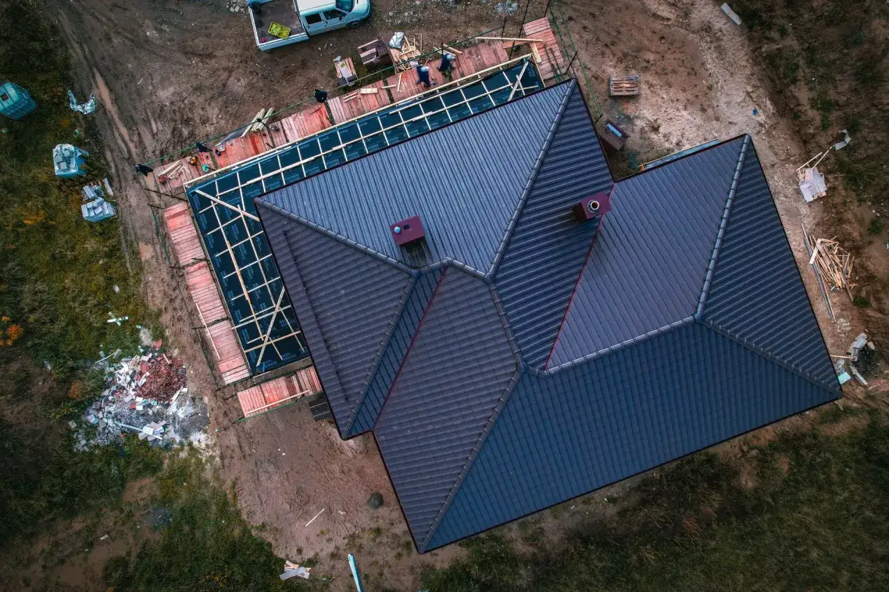Widok z góry na budowę domu z nowym, ciemnym dachem i ekipą budowlaną.