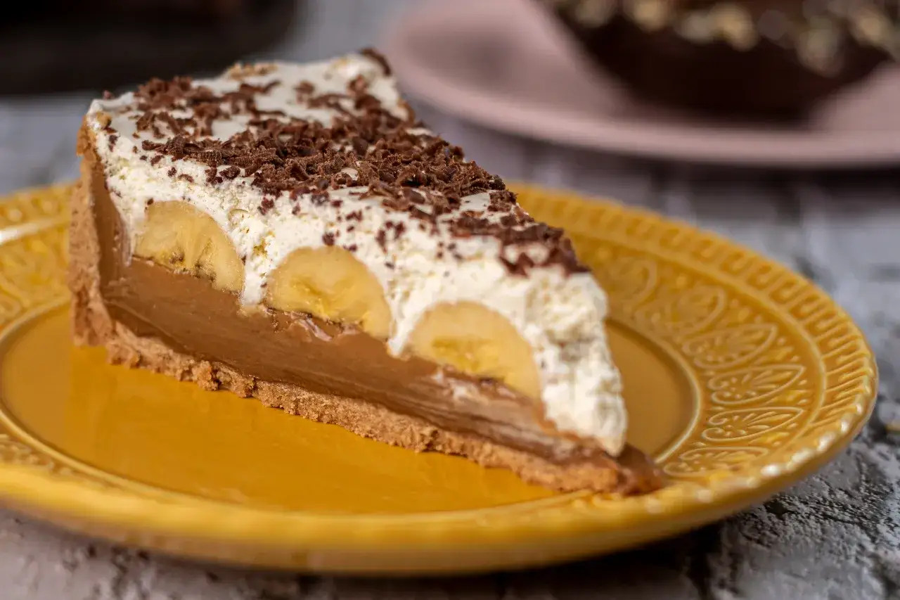 Kawałek banoffee pie z bananami, kremem i czekoladą na żółtym talerzu. Nie tarta cytrynowa, ale pyszny deser!