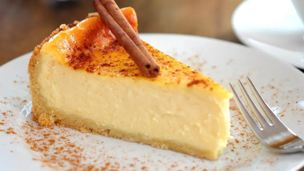 Kawałek sernika na talerzu, ozdobiony laskami cynamonu i posypany cynamonem.