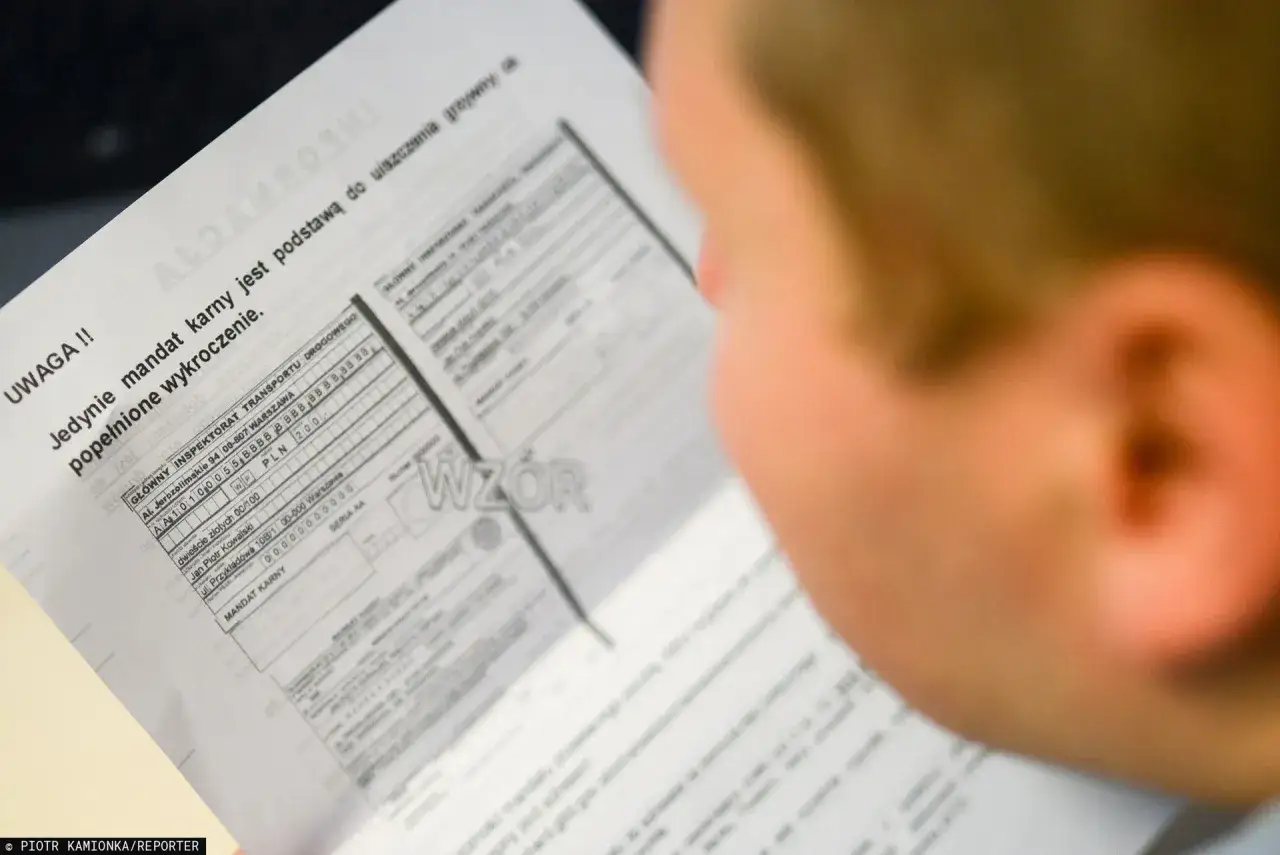 Osoba przygląda się dokumentowi, który pokazuje, jak wygląda mandat z fotoradaru. Widać nagłówek "UWAGA!!" i tekst o podstawie do uiszczenia grzywny.