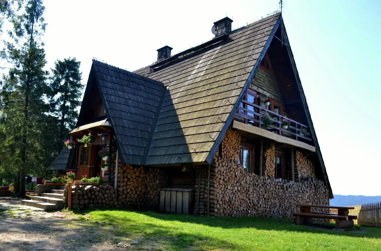 Drewniana bacówka na Turbaczu, z kamiennymi schodami i stosem drewna. Stare wierchy zapraszają do odpoczynku.