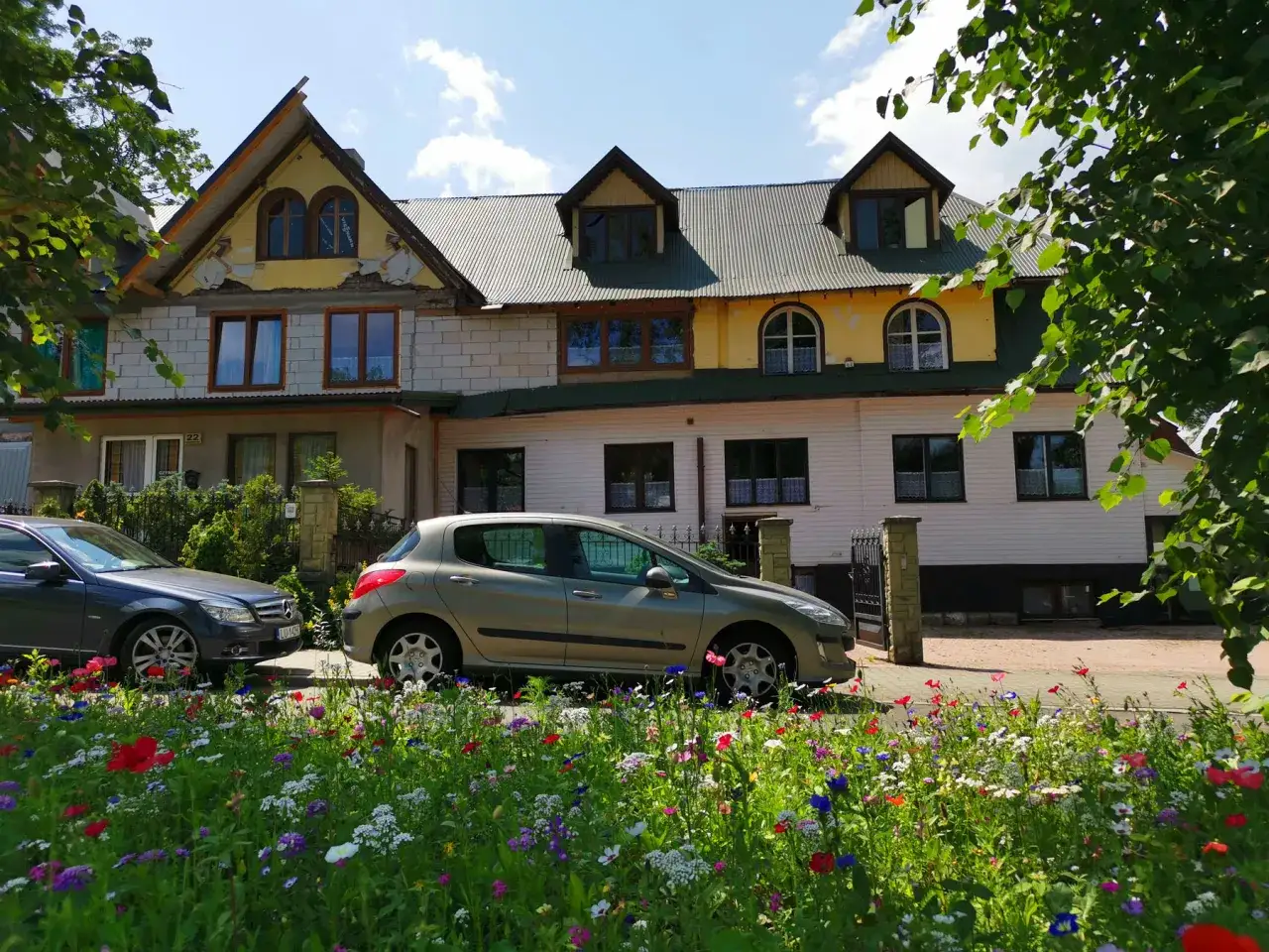 Willa pod zielonym wierchem, z kolorowym ogrodem i samochodami przed wejściem.