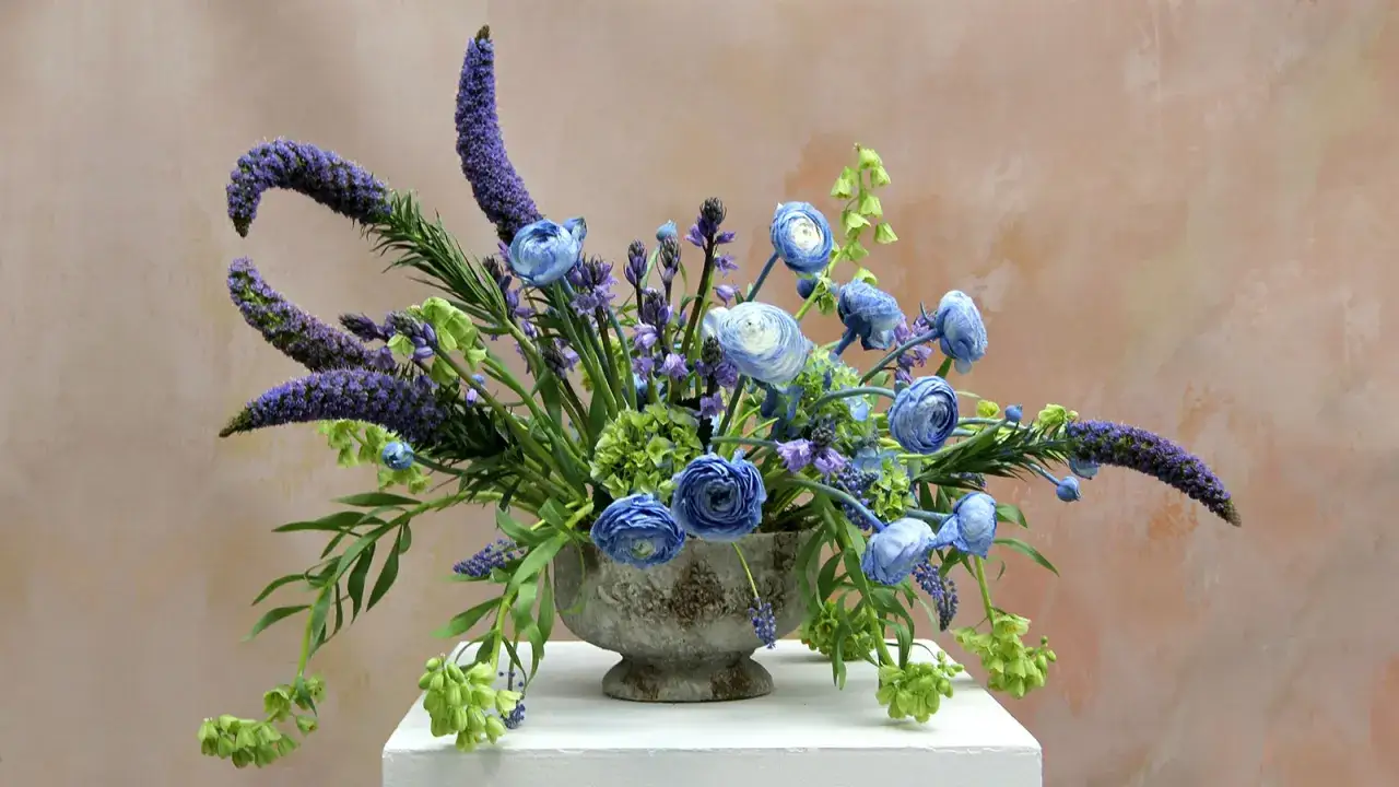 Kompozycja kwiatowa w kamiennym wazonie, z niebieskimi i fioletowymi kwiatami, zielonymi akcentami. Elegancki styl formalny we florystyce.