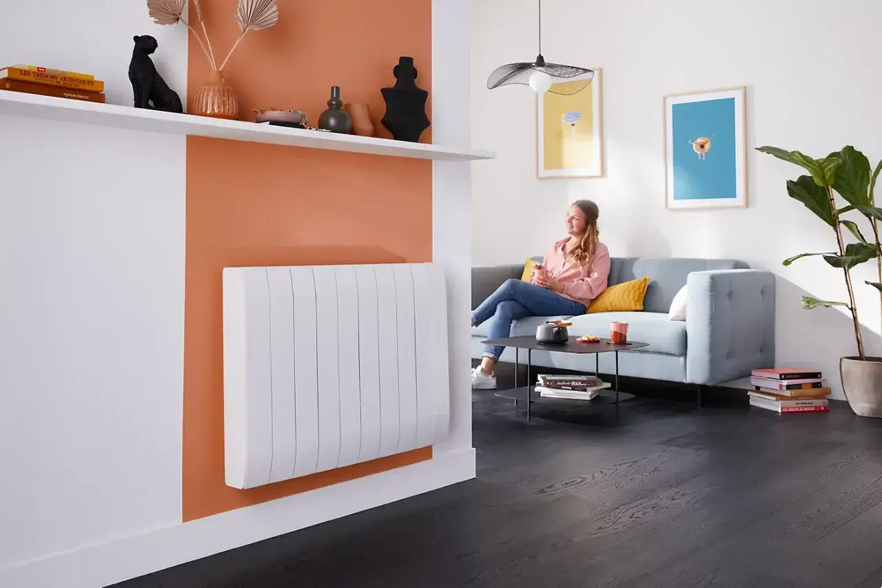 Nowoczesny grzejnik elektryczny to świetny sposób, czym ogrzewać dom. Kobieta siedzi na kanapie, ciesząc się ciepłem.