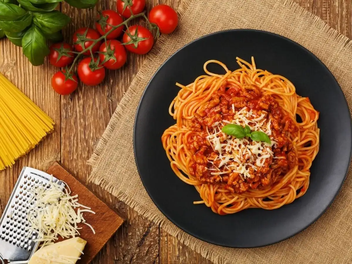 Pyszne spaghetti bolognese na talerzu, z pomidorami i bazylią. Idealne, by dowiedzieć się, jak pasteryzować sos do spaghetti z mięsem mielonym.