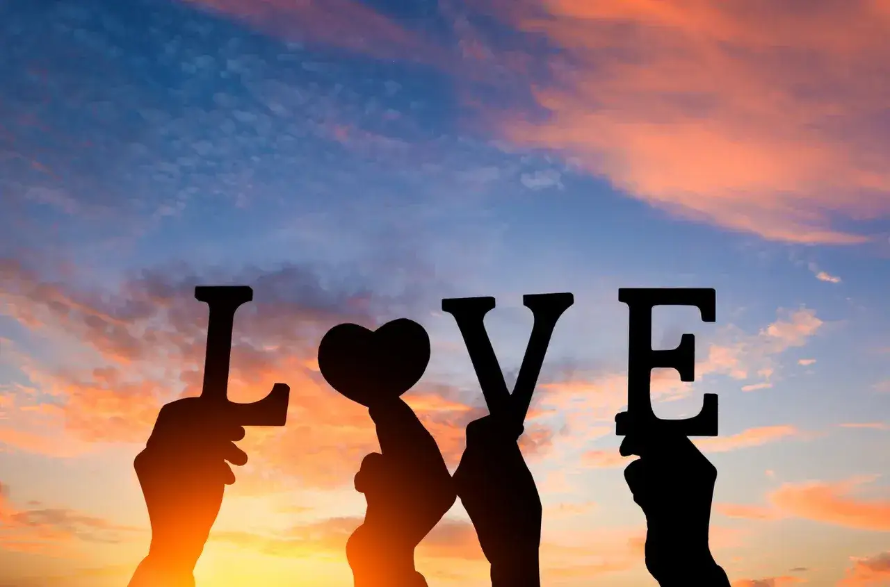 Dłoń trzyma serce, tworząc napis LOVE na tle zachodzącego słońca. To dzień najbardziej kochanych.