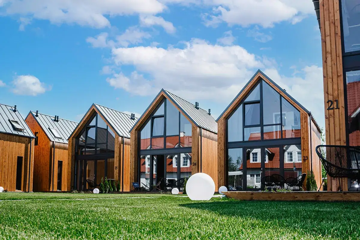 Nowoczesne drewniane domki z dużymi oknami na tle błękitnego nieba z chmurami.