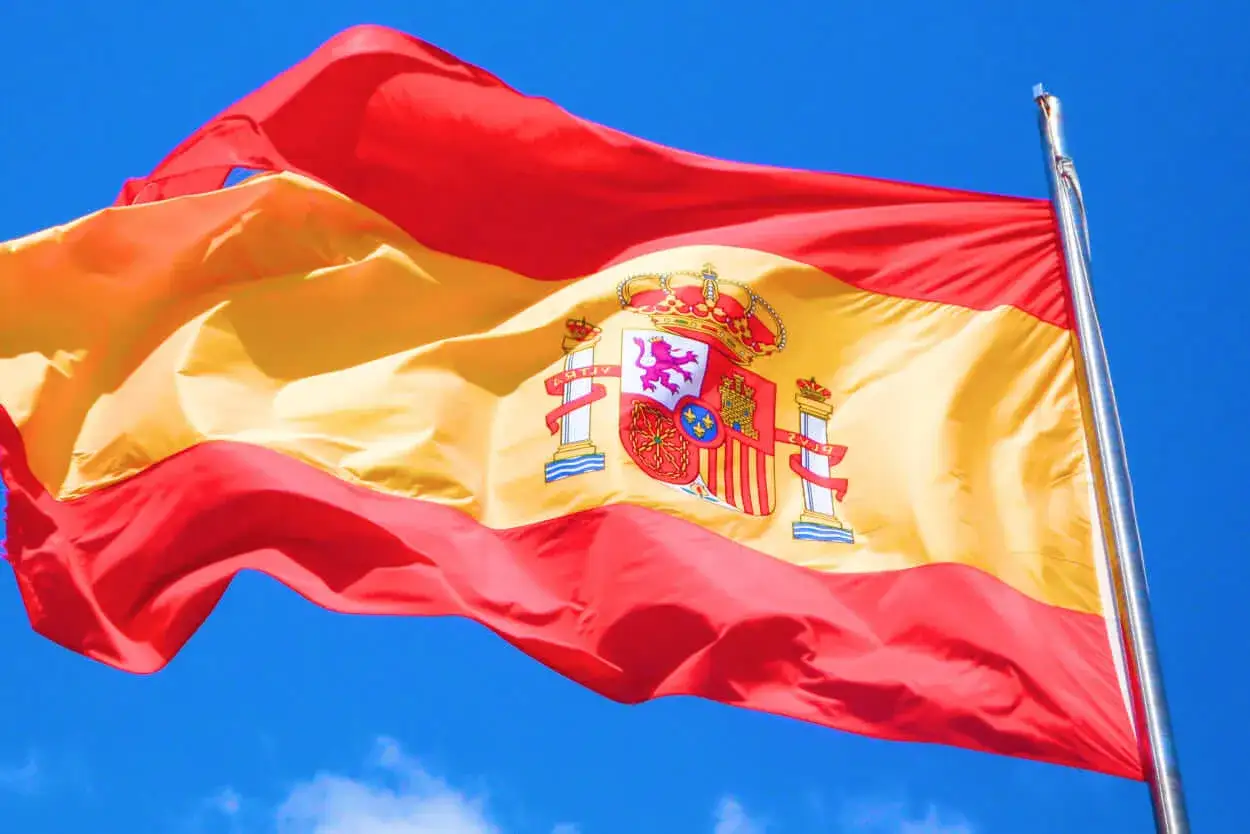 Flaga Hiszpanii powiewa na wietrze na tle błękitnego nieba.