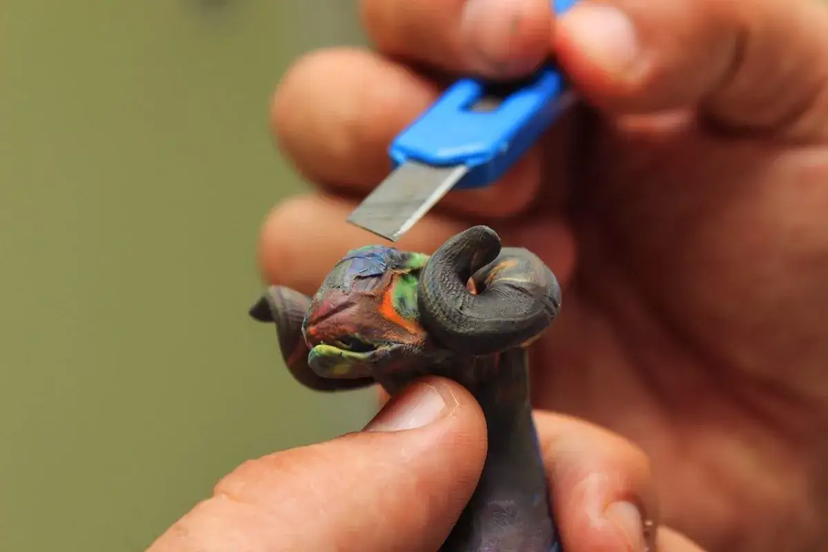 Dłoń precyzyjnie modeluje barwne rzeczy z modeliny, nadając kształt głowie owcy z kręconymi rogami.