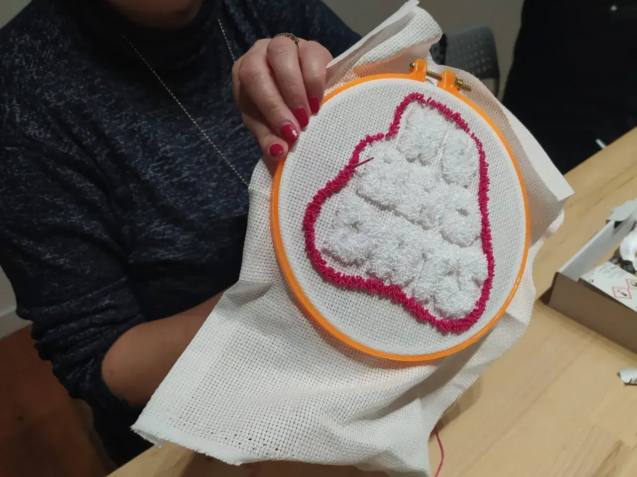 Ręce tworzą biały, puszysty wzór na tamborku, otoczony różowym konturem. To efekt pracy z techniką haft pętelkowy.