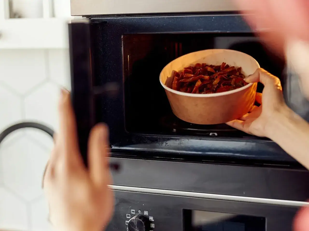 Ręka wkłada miskę z jedzeniem do mikrofalówki. Tak działa mikrofalówka: podgrzewa jedzenie za pomocą fal.