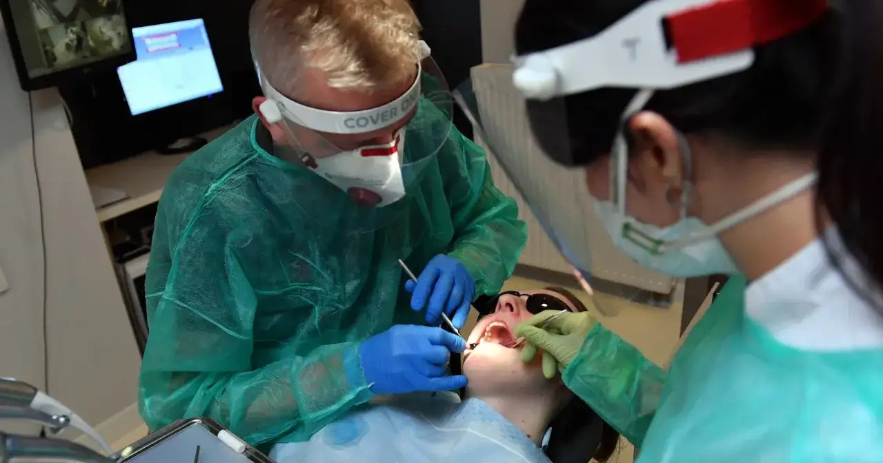 Stomatolodzy w pełnym rynsztunku ochronnym pracują przy pacjencie. To ważny element rejestru zawodów medycznych.