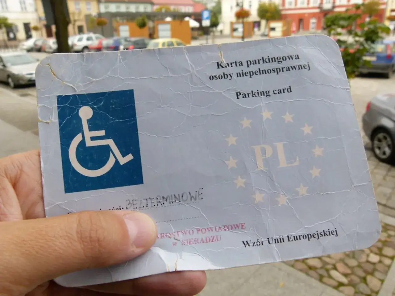 Karta parkingowa osoby niepełnosprawnej z symbolem wózka inwalidzkiego i napisem "PL". Umożliwia korzystanie z miejsca parkingowego dla osób niepełnosprawnych.