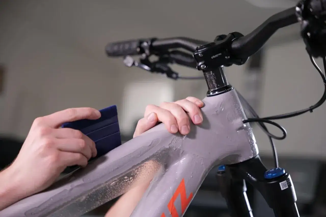 Nakładanie folii ochronnej na ramę roweru. Ręce dociskają niebieski rakiel, rozprowadzając wodę pod folią, zapewniając jej idealne przyleganie.