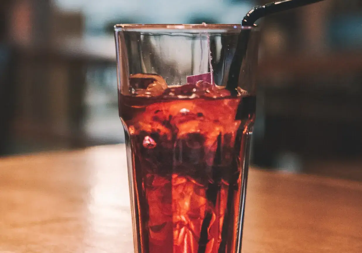 Szklanka z lodem i ciemnym napojem, idealne proporcje whisky z colą. Czarna słomka zanurzona w napoju.